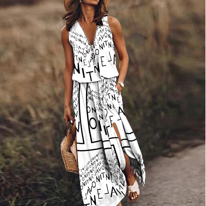 Vrouw in witte zomerjurk met zwarte letters, draagt een strooien tas en sandalen, staat buiten op een pad. Trendy damesmode, casual zomeroutfit.