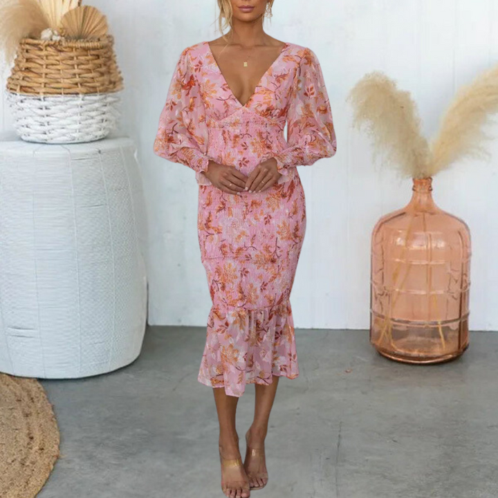 Vrouw in roze bloemenjurk met lange mouwen, staand voor decoratieve mand en vaas. Elegante zomerjurk, boho-stijl, modetrend 2023.