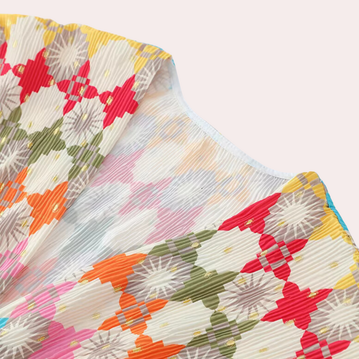 Plissé stof met kleurrijk geometrisch patroon, waaronder rode, groene en oranje vormen. Ideaal voor modeontwerp en interieurdecoratie.