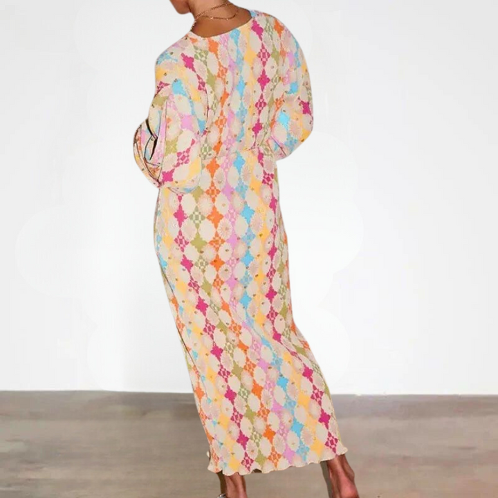 Vrouw in kleurrijke, lange jurk met geometrisch patroon, staand op houten vloer. Trendy damesmode, bohemian stijl, comfortabele pasvorm.