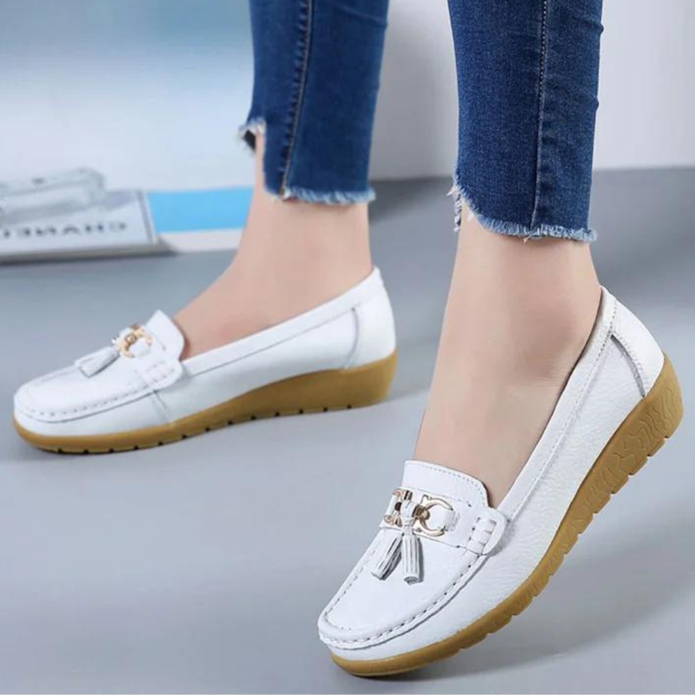 Witte leren loafers met gouden details en bruine zool, gedragen door model in blauwe jeans. Comfortabele damesschoenen, modieus en stijlvol.
