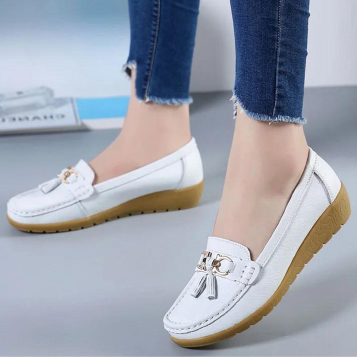 Witte leren loafers met gouden details en bruine zool, gedragen door model in blauwe jeans. Comfortabele damesschoenen, modieus en stijlvol.