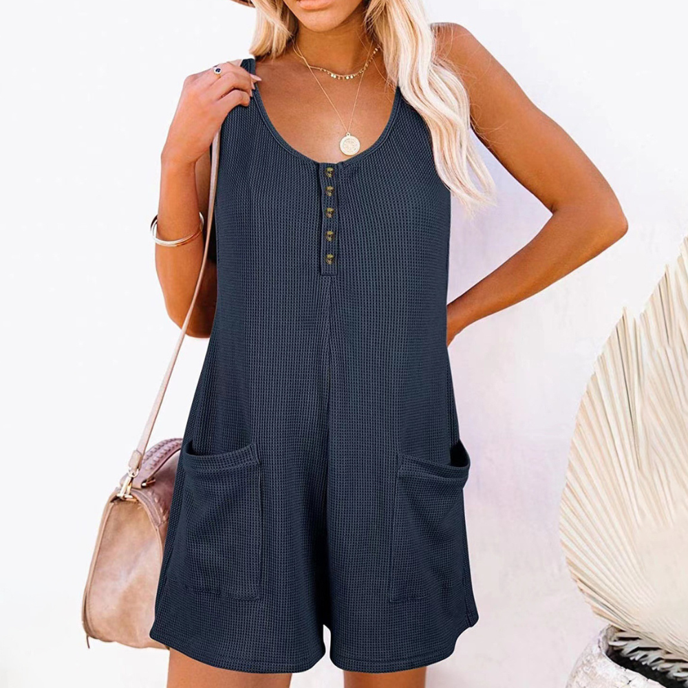 Vrouw in donkerblauwe zomerse playsuit met knoopsluiting en zakken, draagt een beige hoed en tas. Perfect voor casual zomeroutfits.