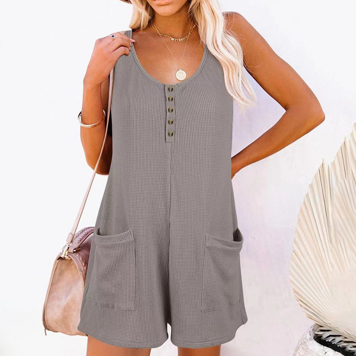 Vrouw in grijze zomerse playsuit met knoopsluiting en zakken, strandtas over schouder, blonde golvende haren, casual zomeroutfit.