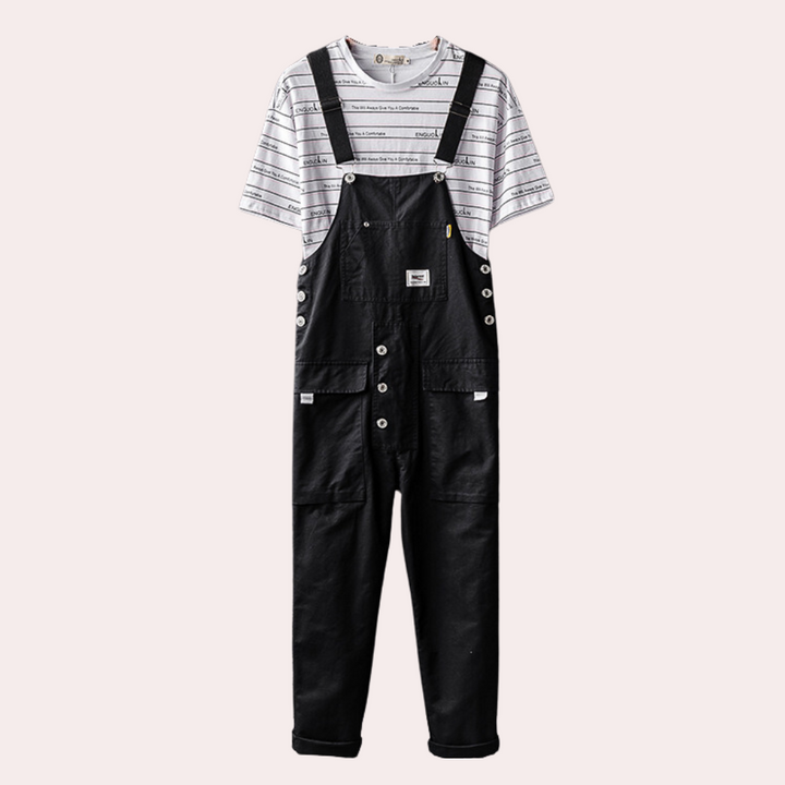 Zwarte denim overall met knopen en zakken, gedragen over een gestreept T-shirt. Modieuze unisex kleding, casual stijl, comfortabele pasvorm.
