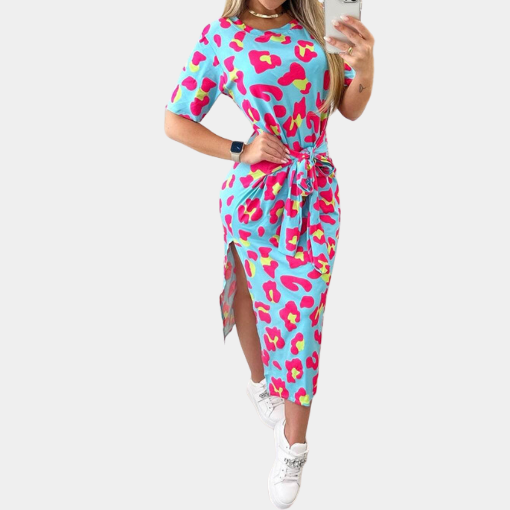 Vrouw in blauwe jurk met kleurrijke luipaardprint, korte mouwen en ceintuur, poseert met smartphone. Trendy damesmode, casual stijl.