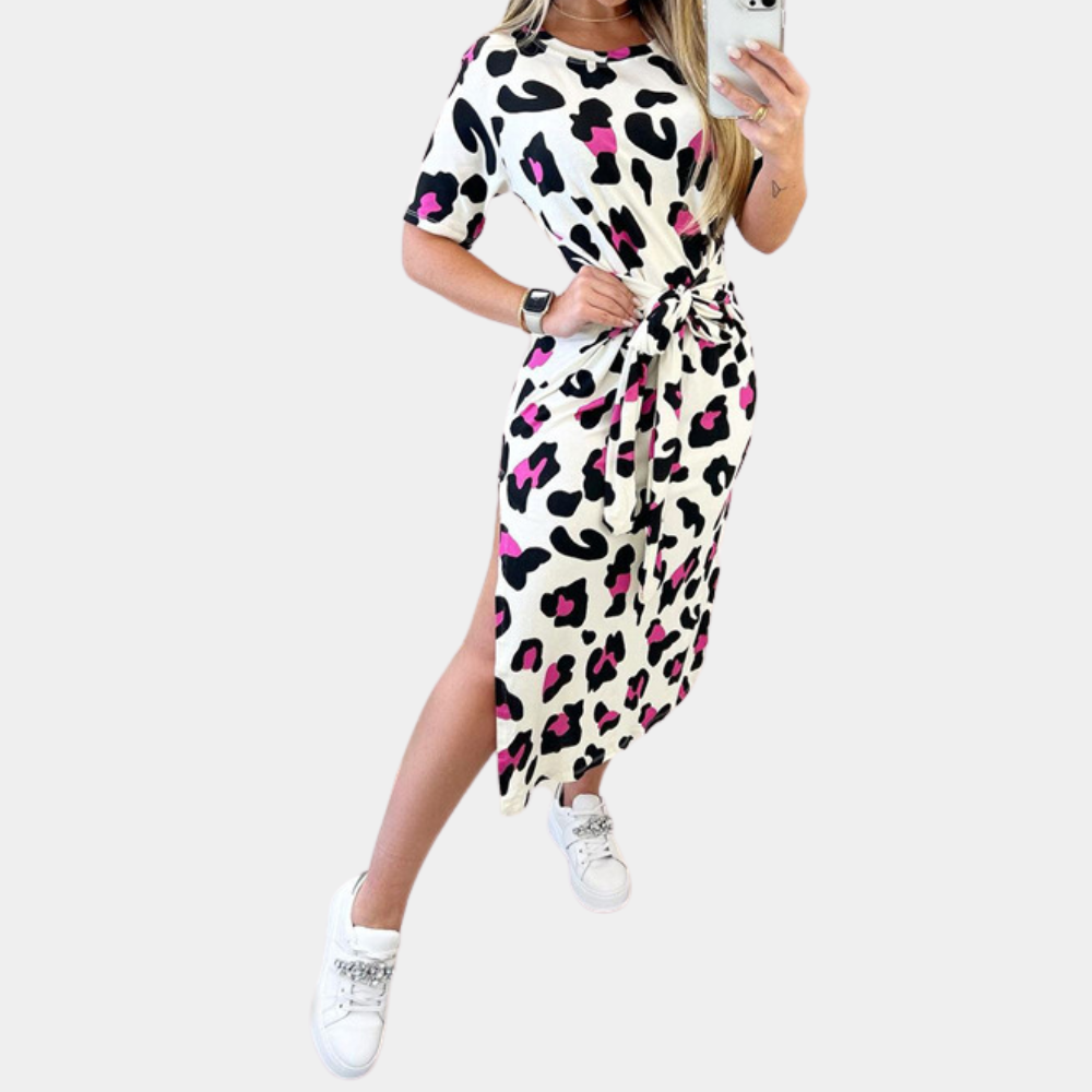 Vrouw in wit-zwarte luipaardprint jurk met roze accenten, korte mouwen en zijslit, draagt witte sneakers. Modieuze dameskleding, casual stijl.