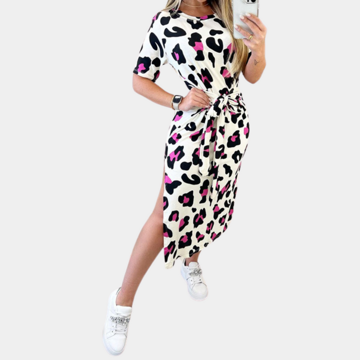 Vrouw in wit-zwarte luipaardprint jurk met roze accenten, korte mouwen en zijslit, draagt witte sneakers. Modieuze dameskleding, casual stijl.