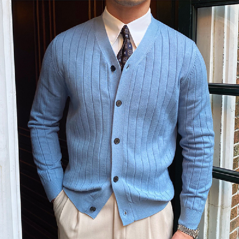 Man in lichtblauw geribd vest met knopen, witte overhemd en stropdas, voor een deur. Stijlvolle herenkleding, klassieke mode, elegante outfit.