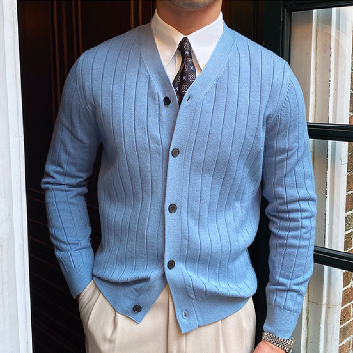 Man in lichtblauw geribd vest met knopen, witte overhemd en stropdas, voor een deur. Stijlvolle herenkleding, klassieke mode, elegante outfit.