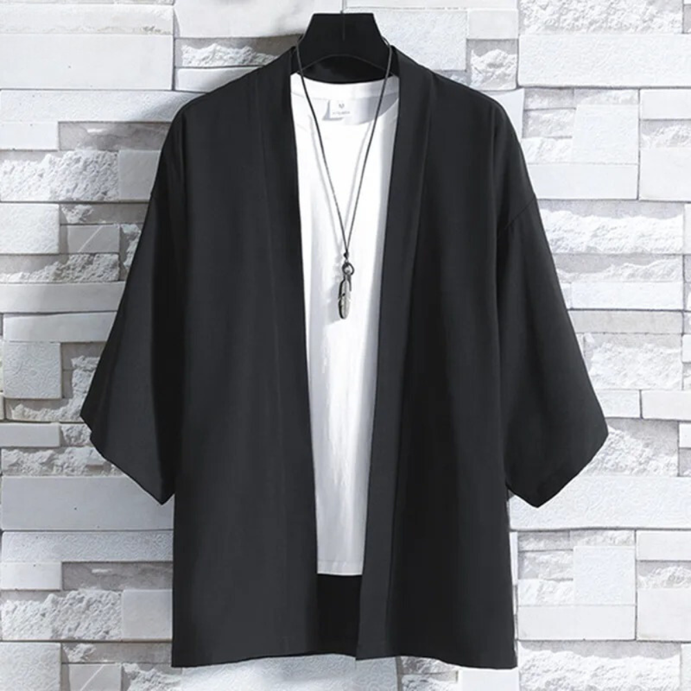 Zwarte kimono jas voor heren, casual stijl, driekwart mouwen, opgehangen voor een witte bakstenen muur. Perfect voor moderne, minimalistische mode.