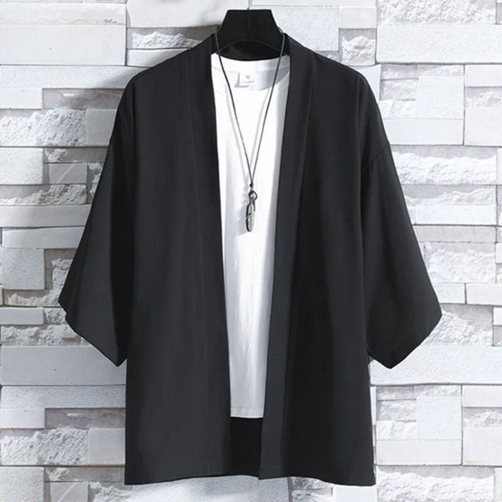 Zwarte kimono jas voor heren, casual stijl, driekwart mouwen, opgehangen voor een witte bakstenen muur. Perfect voor moderne, minimalistische mode.