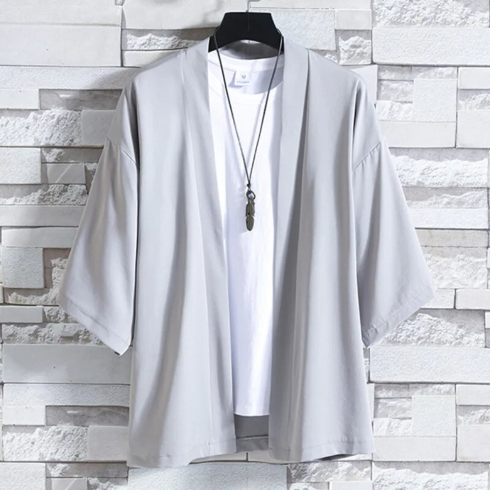 Lichtgrijze kimono jas voor heren, casual stijl, opgehangen aan een hanger tegen een stenen muur. Perfect voor moderne, minimalistische mode.