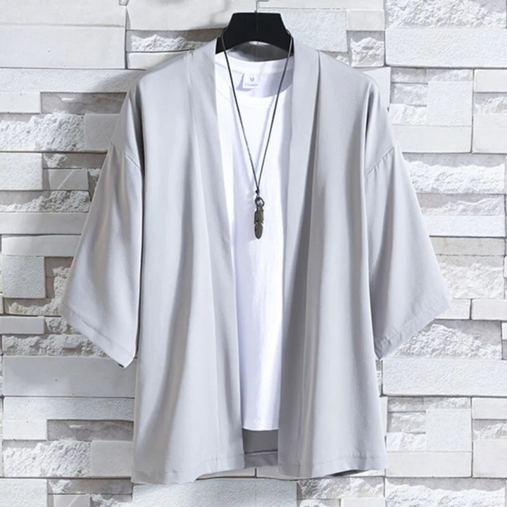 Lichtgrijze kimono jas voor heren, casual stijl, opgehangen aan een hanger tegen een stenen muur. Perfect voor moderne, minimalistische mode.