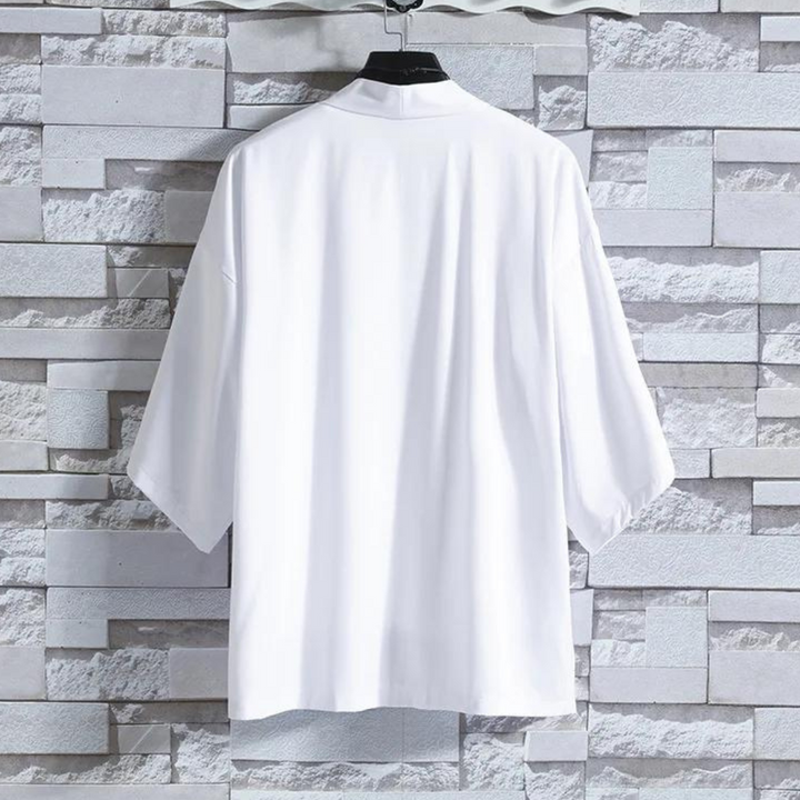 Witte katoenen blouse met driekwart mouwen, hangend aan een hanger tegen een grijze bakstenen muur. Stijlvolle damesmode, minimalistisch design.