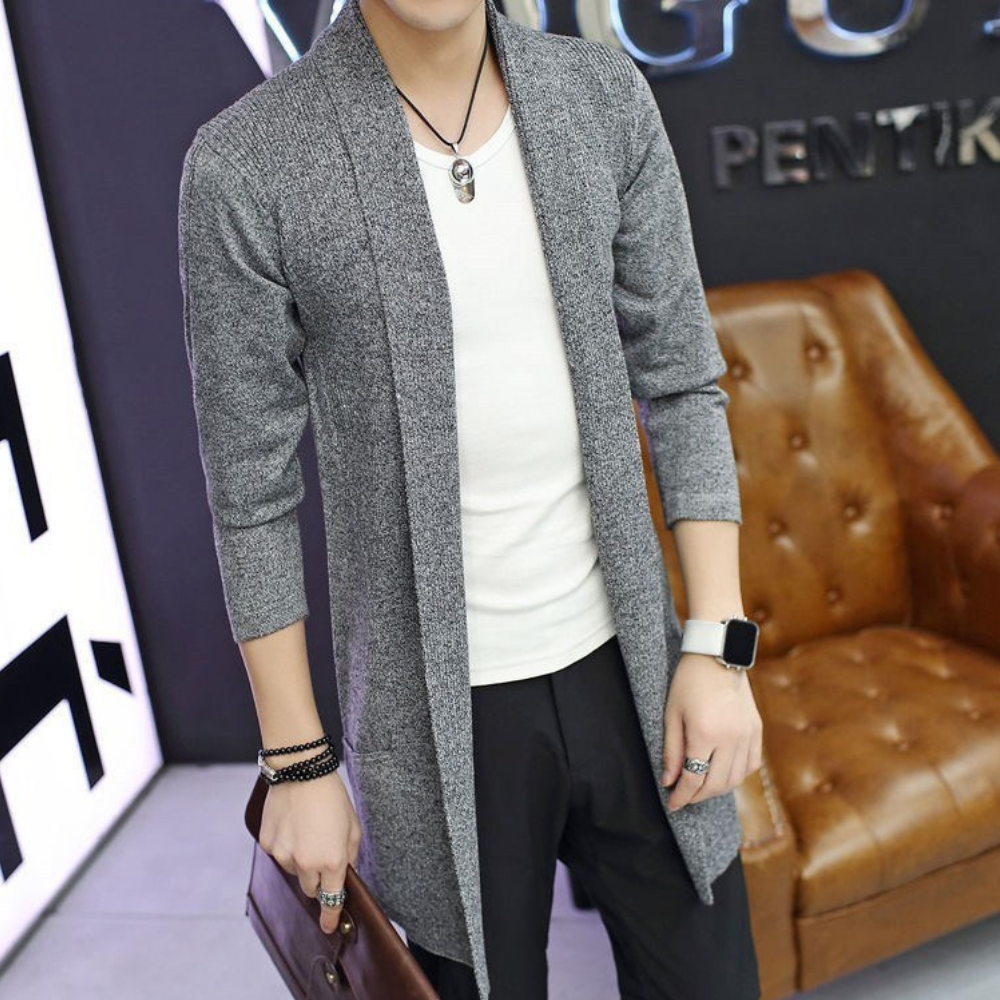 Grijze lange cardigan voor heren, gedragen over een wit T-shirt. Stijlvolle casual outfit met accessoires zoals een horloge en armband.