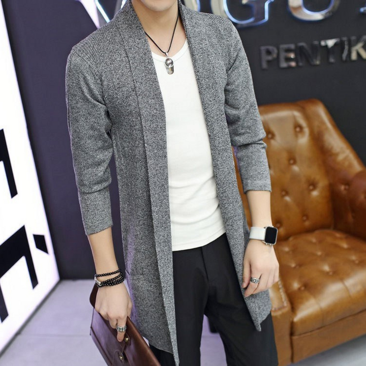 Grijze lange cardigan voor heren, gedragen over een wit T-shirt. Stijlvolle casual outfit met accessoires zoals een horloge en armband.