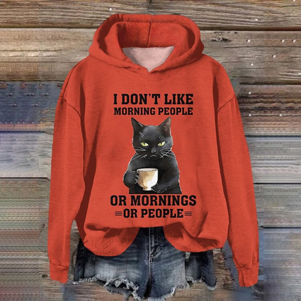 Rode hoodie met zwarte kat en tekst "I don't like morning people or mornings or people", opgehangen voor houten achtergrond, casual mode.