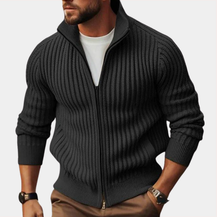 Zwarte gebreide herenvest met ritssluiting, gedragen over een wit T-shirt. Stijlvolle casual outfit, perfect voor herfst- en wintermode.