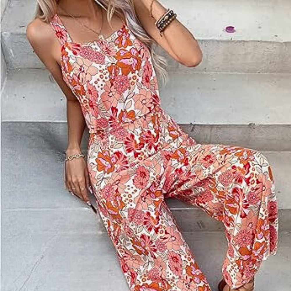 Vrouw in kleurrijke, oranje bloemen jumpsuit zittend op trap. Trendy zomeroutfit, bohemian stijl, casual mode, dameskleding.