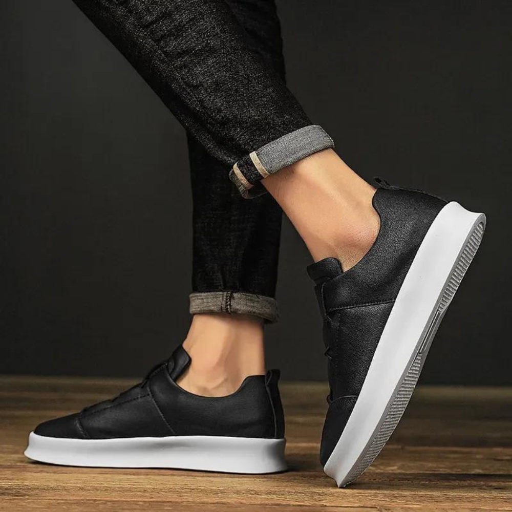 Zwarte leren sneakers met witte zool, gedragen door persoon in opgerolde jeans. Stijlvolle casual schoenen voor heren, perfect voor dagelijks gebruik.