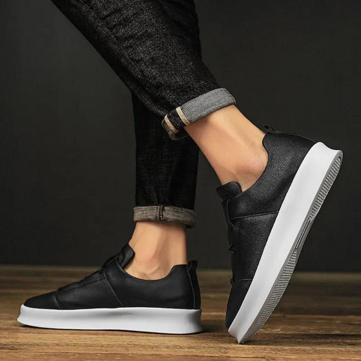 Zwarte leren sneakers met witte zool, gedragen door persoon in opgerolde jeans. Stijlvolle casual schoenen voor heren, perfect voor dagelijks gebruik.