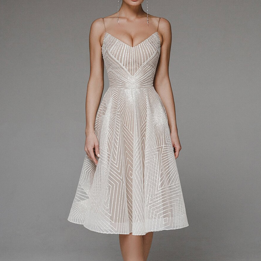 Vrouw in elegante witte cocktailjurk met geometrisch patroon, V-hals en spaghetti bandjes. Perfect voor feestelijke gelegenheden.