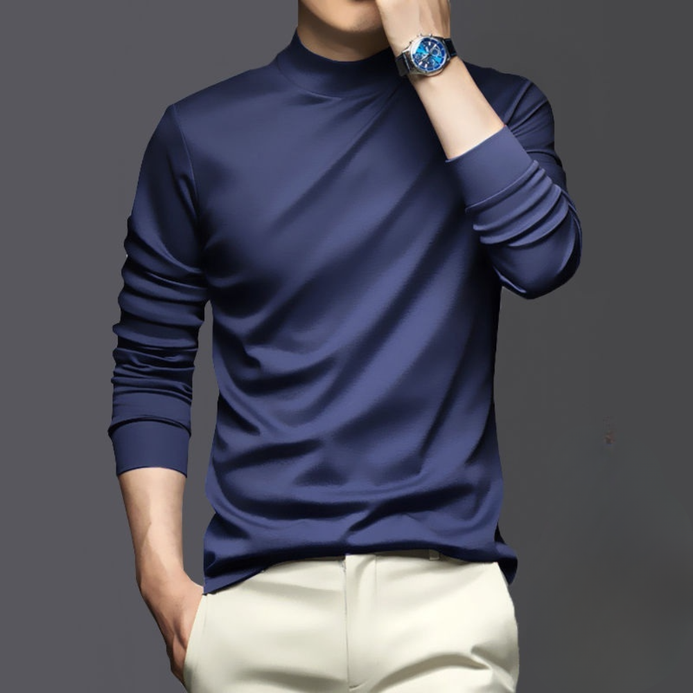 Man in donkerblauwe coltrui met opgerolde mouwen, draagt een luxe blauw horloge, poseert tegen een grijze achtergrond. Stijlvolle herenkleding.