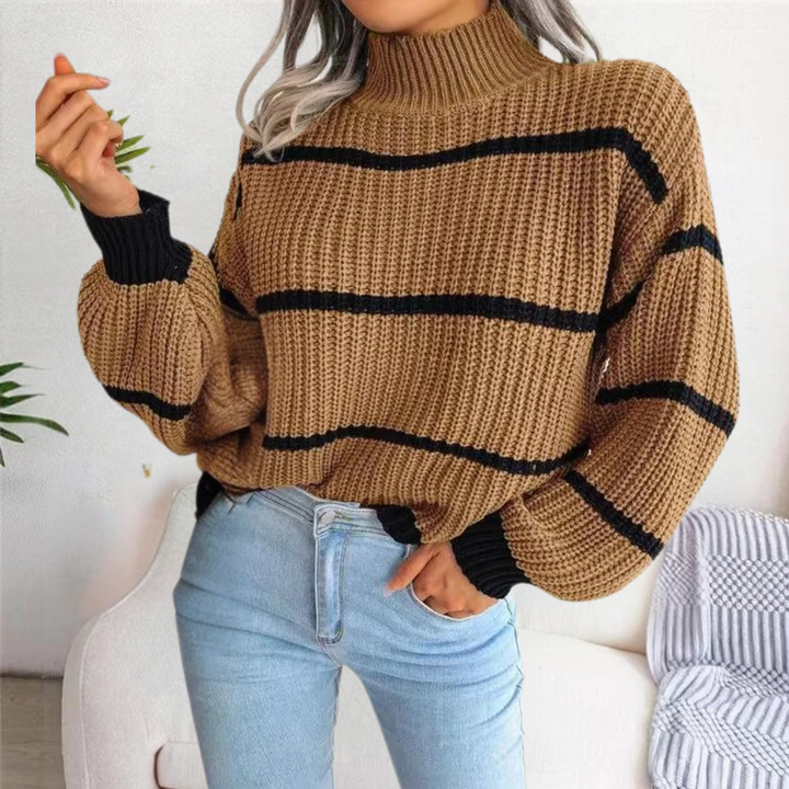Vrouw in beige gebreide trui met zwarte strepen, hoge kraag en lange mouwen, gecombineerd met lichtblauwe jeans. Trendy herfstmode.
