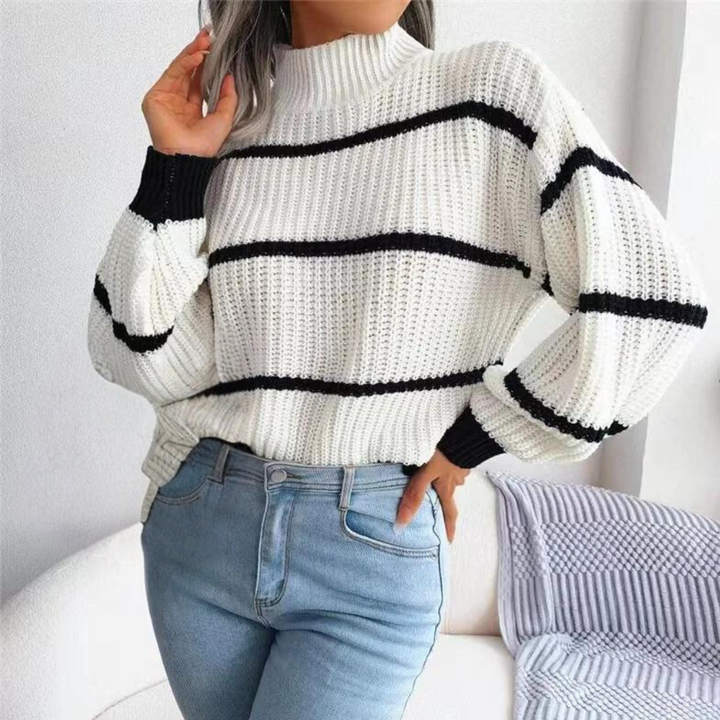 Vrouw draagt witte gebreide trui met zwarte strepen, gecombineerd met blauwe jeans. Modieuze dameskleding, herfst-winter stijl, casual outfit.
