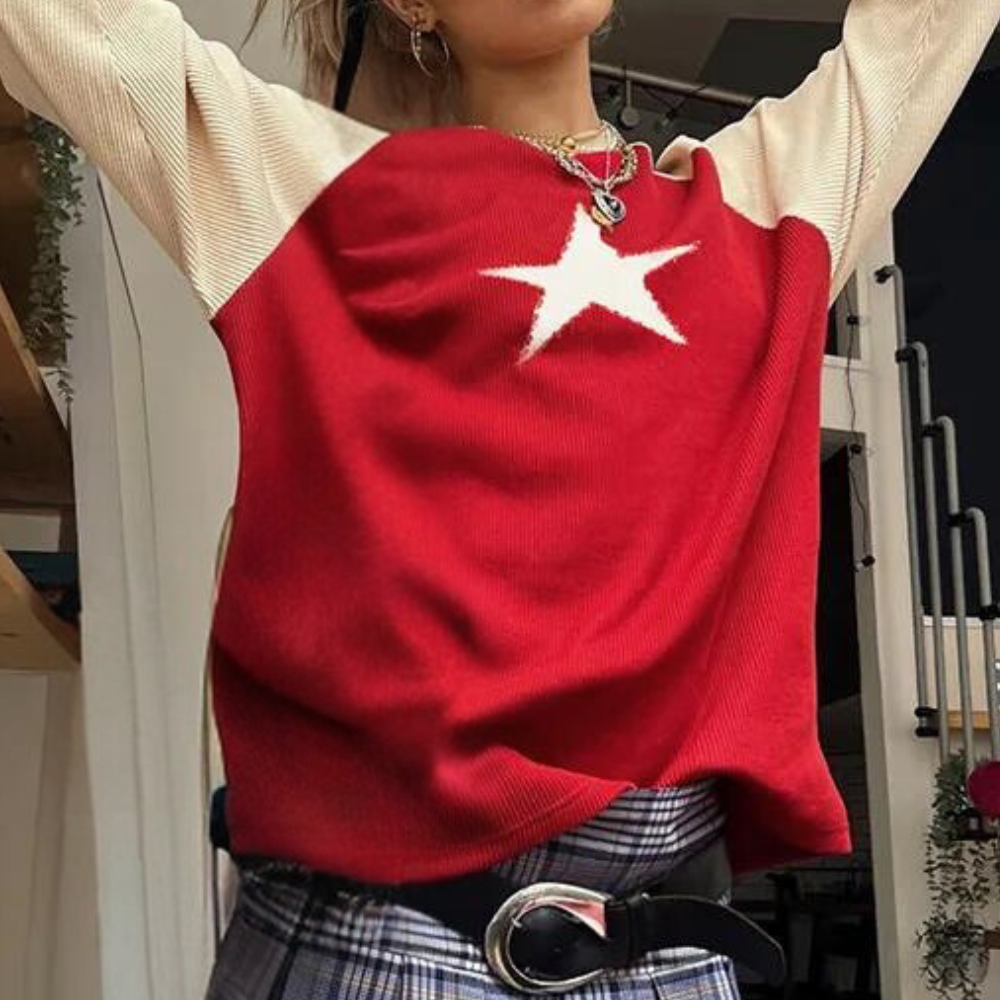Rode trui met witte ster, lange mouwen en geribbelde textuur, gedragen door persoon. Modieuze outfit met geruite broek en zilveren riem.