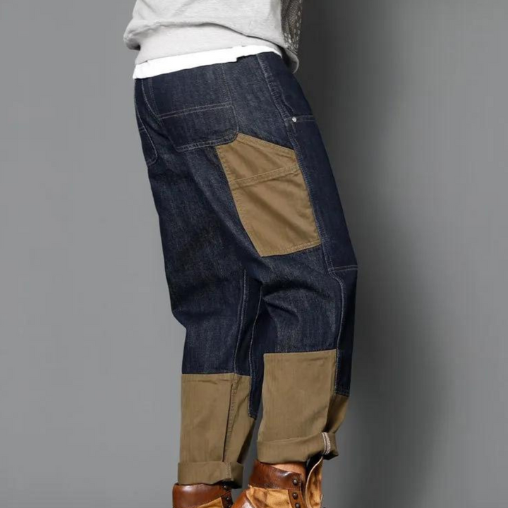 Donkerblauwe denim werkbroek met bruine kniestukken en zakken, gedragen door een persoon. Ideaal voor casual en outdoor activiteiten.