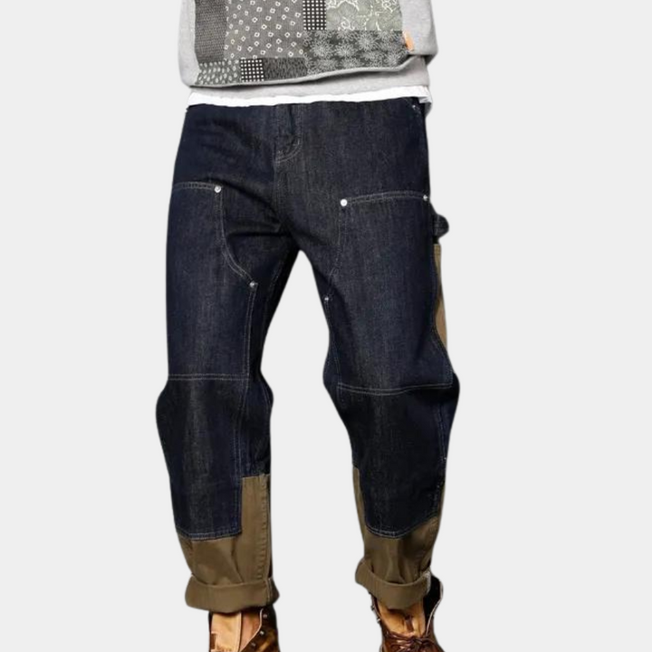Donkerblauwe denim werkbroek met bruine kniestukken en zakken, ideaal voor casual en outdoor activiteiten. Comfortabele pasvorm, duurzame stof.