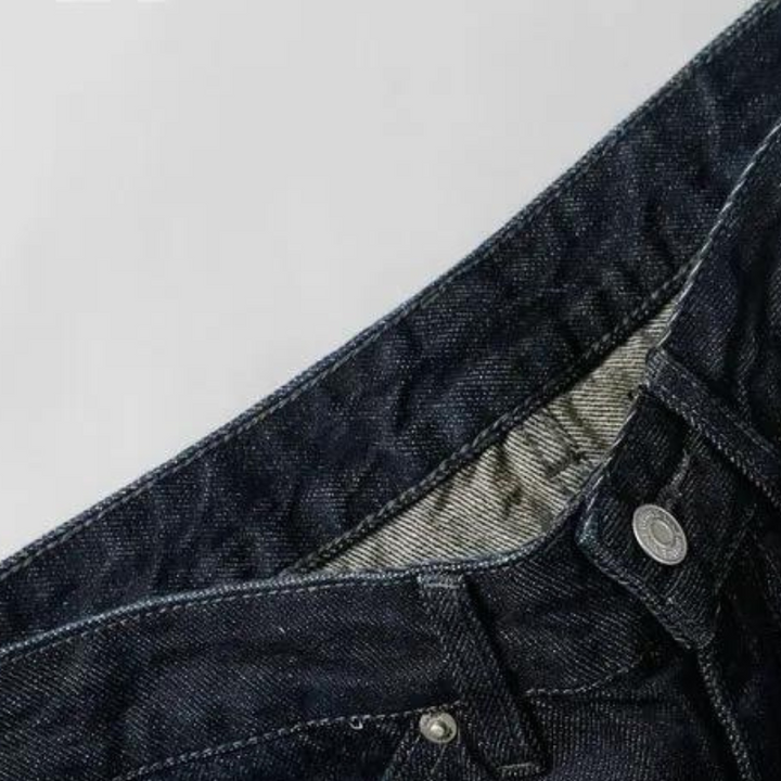 Donkerblauwe denim jeans met zichtbare knopen en stiksels, close-up. Modieuze spijkerbroek, casual kleding, hoogwaardige stof.