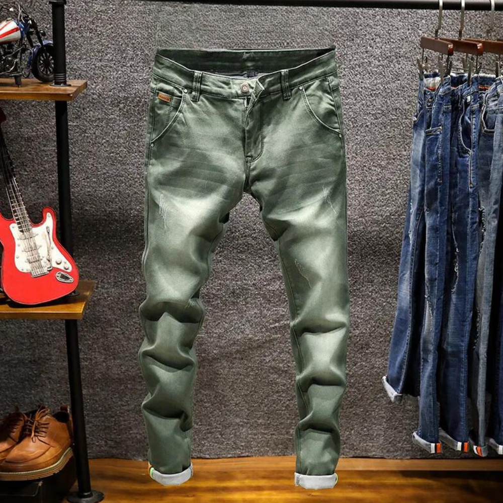 Donkergroene herenjeans opgehangen in een kledingwinkel, naast een rode gitaar en andere spijkerbroeken. Modieuze casual broek voor mannen.