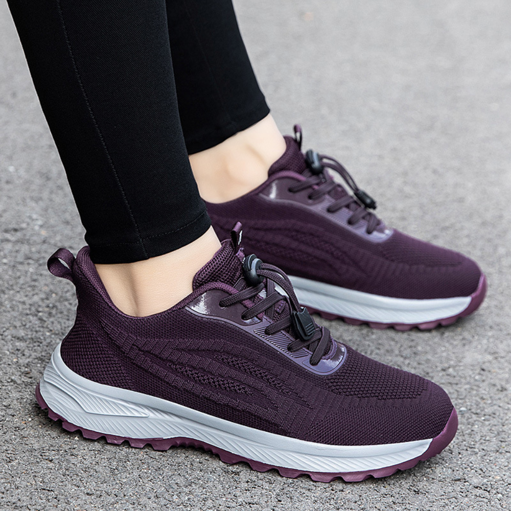 Donkerpaarse sportschoenen met witte zool, gedragen door persoon op grijze ondergrond. Comfortabele sneakers voor hardlopen en wandelen.