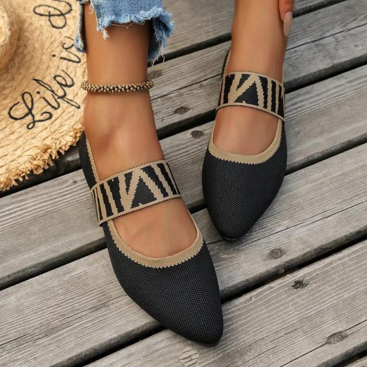Zwarte damesballerina's met geometrisch patroon, puntige neus en elastische band, gedragen op houten vloer. Trendy zomerschoenen, casual stijl.