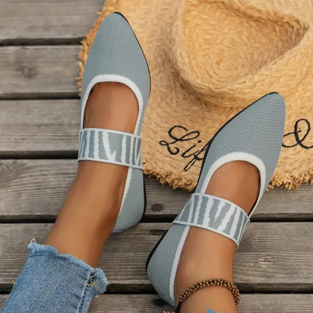 Lichtgrijze damesballerina's met gestreepte band, gedragen met jeans op houten vloer, naast strohoed. Comfortabele en stijlvolle schoenen.