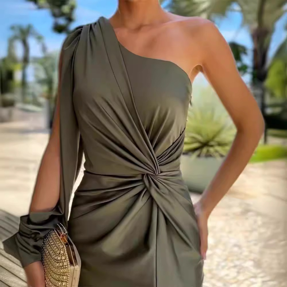 Vrouw in elegante, asymmetrische groene jurk met knoopdetail, buiten gefotografeerd. Perfect voor zomerfeesten. Luxe mode, stijlvolle avondkleding.