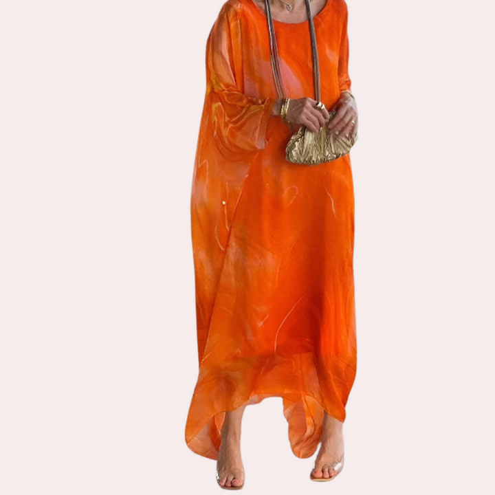 Oranje damesjurk met lange mouwen, vloeiende stof en abstract patroon. Perfect voor zomeravonden. Accessoires: gouden clutch en ketting.