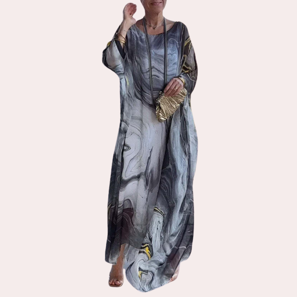 Vrouw in lange, vloeiende jurk met marmerprint en gouden clutch. Modieuze dameskleding, elegante avondjurk, trendy accessoires.