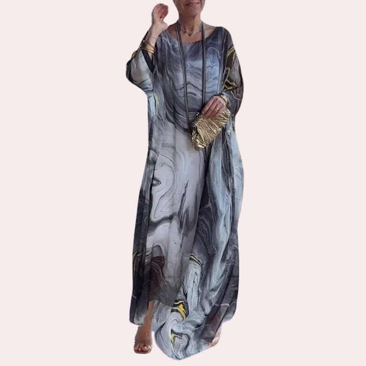Vrouw in lange, vloeiende jurk met marmerprint en gouden clutch. Modieuze dameskleding, elegante avondjurk, trendy accessoires.