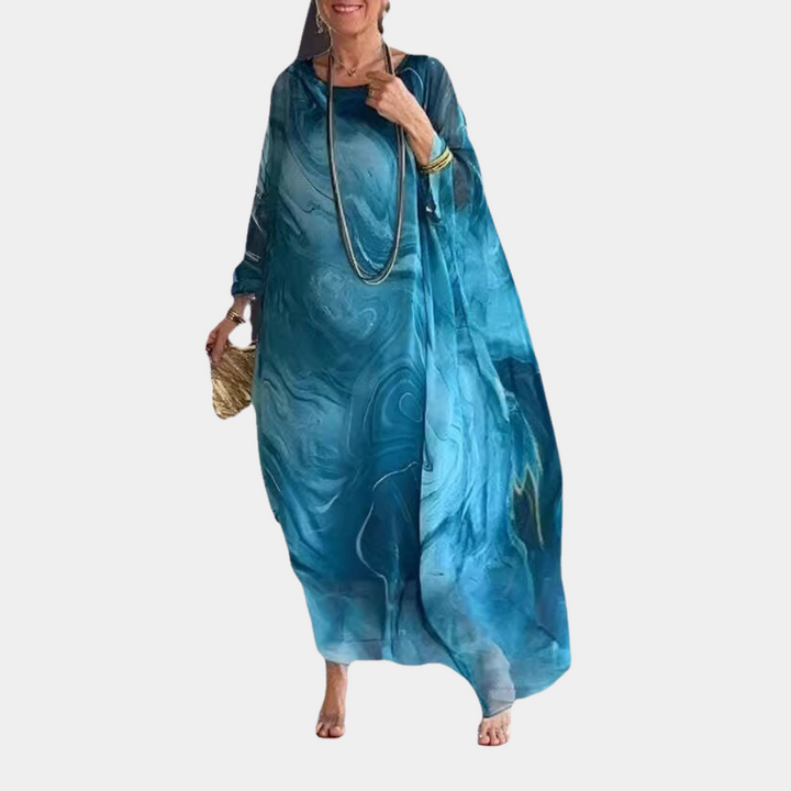 Vrouw in elegante blauwe kaftan jurk met marmerpatroon, gouden sieraden en rieten tas. Modieuze dameskleding, bohemian stijl.