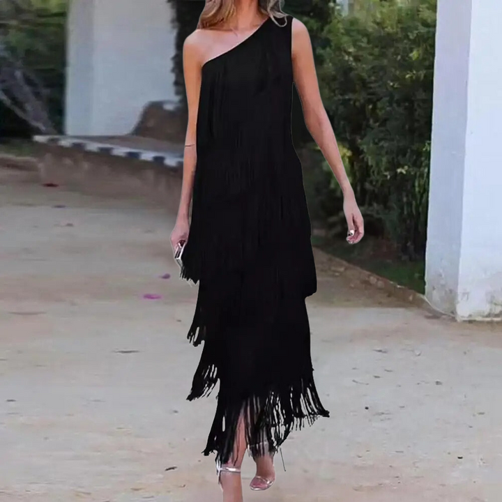 Elegante zwarte asymmetrische jurk met franjes, perfect voor avondfeesten. Vrouw draagt stijlvolle hakken, buitenomgeving op achtergrond.