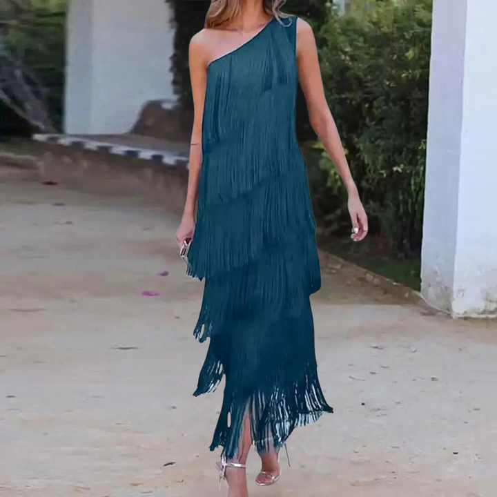 Vrouw in groene asymmetrische jurk met franjes, buiten op een zonnige dag. Trendy mode, elegante avondjurk, zomeroutfit.