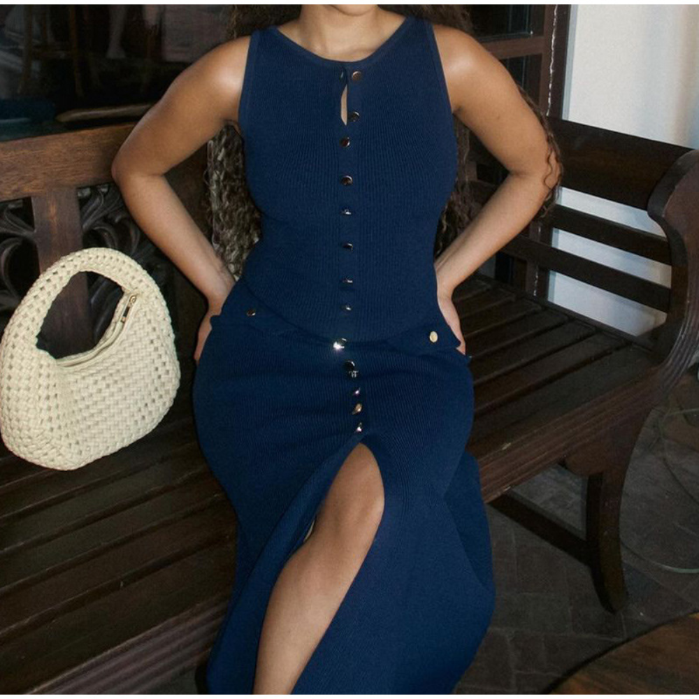 Vrouw in elegante blauwe jurk met knoopsluiting, zittend op houten bank. Witte gevlochten tas naast haar. Mode, zomerjurk, dameskleding.