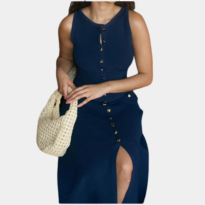Vrouw in marineblauwe jurk met knoopsluiting en split, houdt een beige gevlochten tas vast. Elegante damesmode, zomerjurk, casual chique stijl.