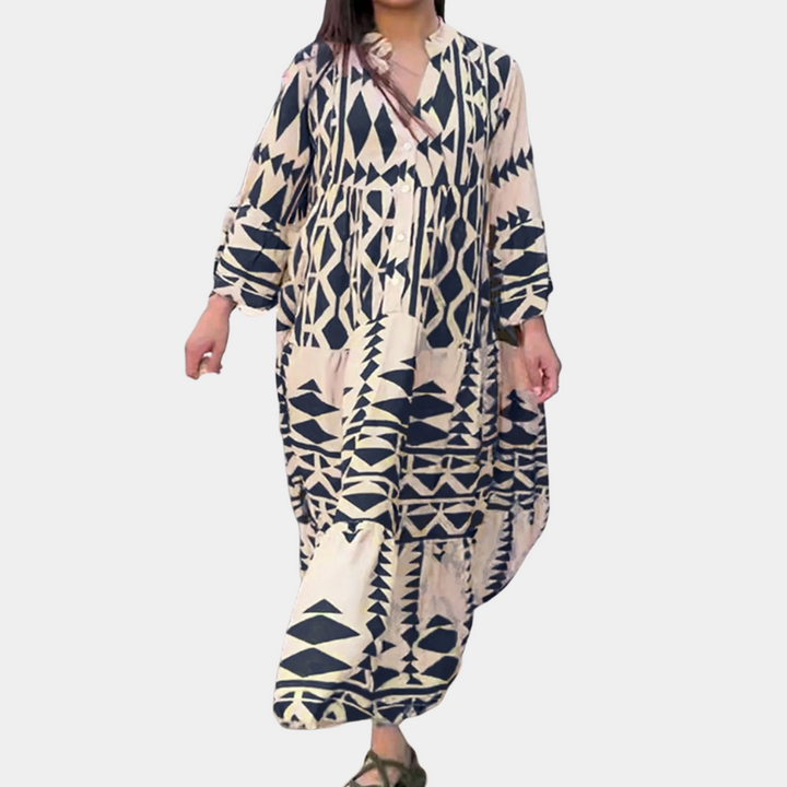 Vrouw in lange, blauwe en witte geometrische printjurk, boho-stijl, met lange mouwen. Perfect voor casual zomeroutfits en strandmode.