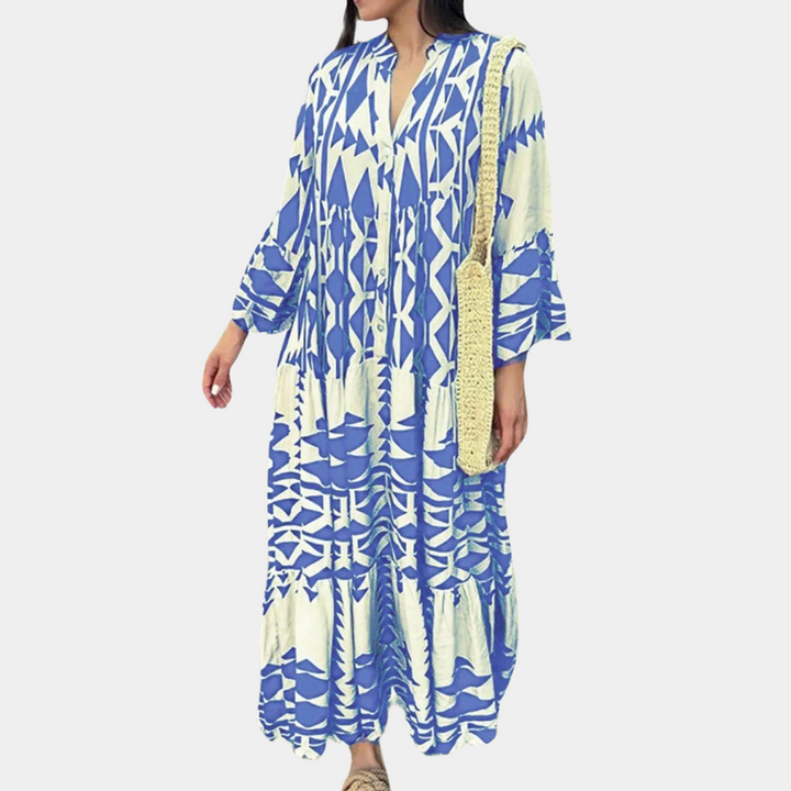 Vrouw in lange blauwe en witte jurk met geometrisch patroon, draagt een strooien schoudertas. Modieuze zomerjurk, bohemian stijl.
