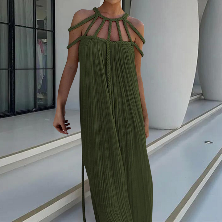 Vrouw in stijlvolle, groene maxi-jurk met open schouders en gevlochten details, staand voor moderne architectuur. Perfect voor zomer- en avondmode.